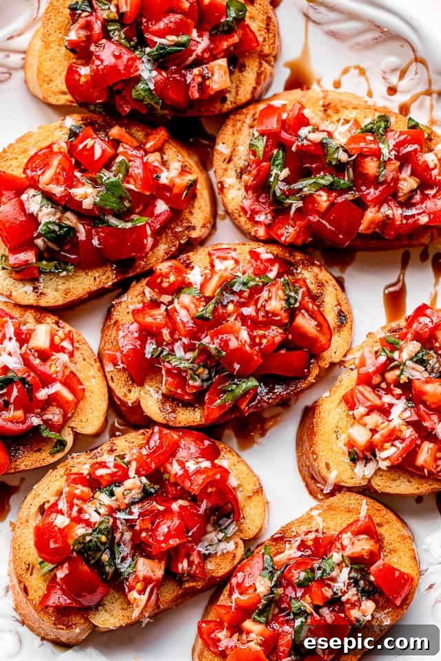 Toasted garlic bread slices generously topped with a fresh balsamic tomato salad, served on a pristine white platter.