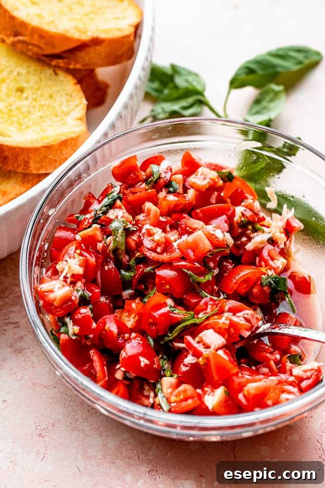 A vibrant bowl of fresh tomato salad, rich with basil, garlic, and parmesan, sits beside golden garlic bread slices.