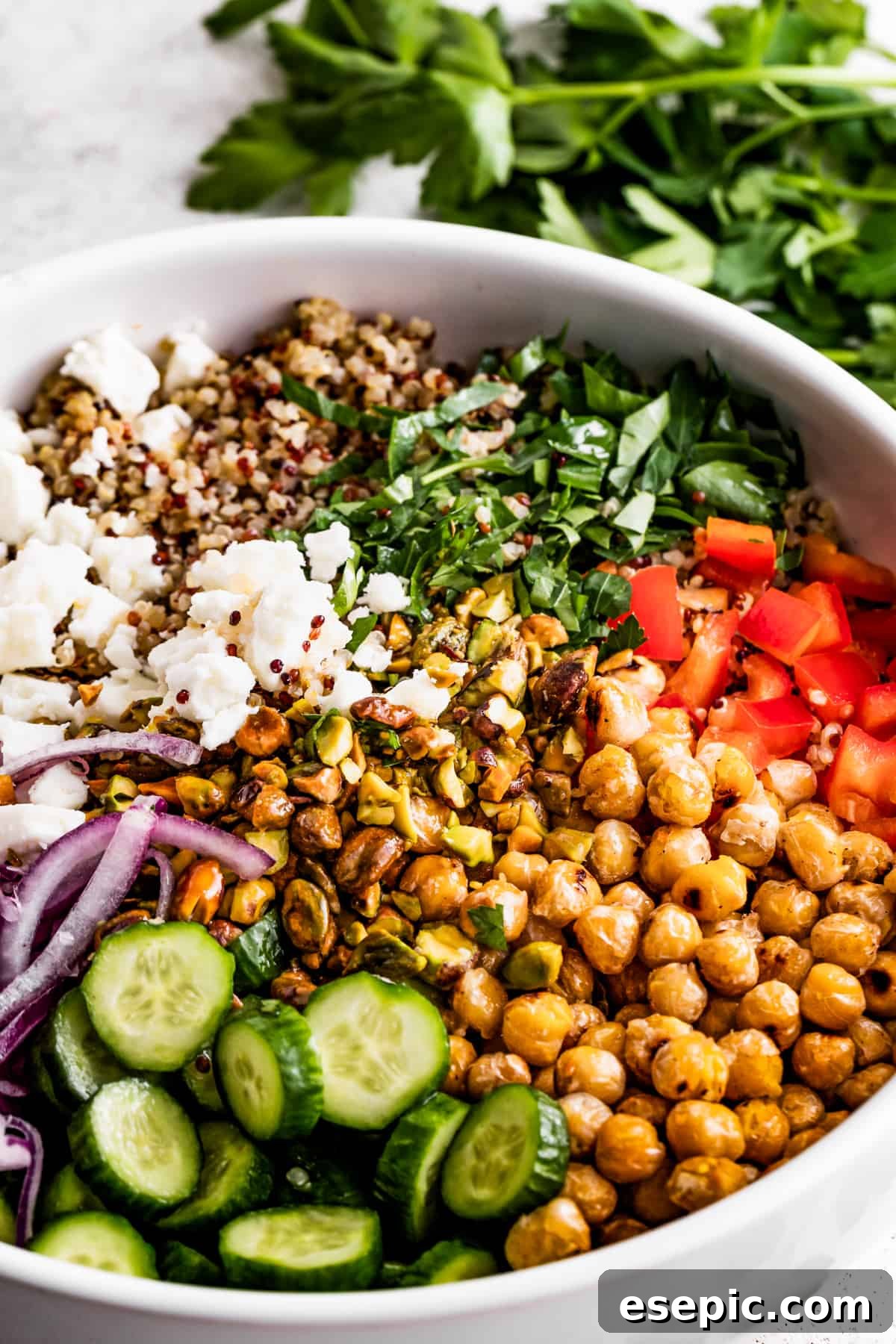 A large bowl of the Jennifer Aniston salad, brimming with colorful ingredients like cucumbers, red onions, chickpeas, bell peppers, fresh herbs, tri-colored quinoa, and crumbled feta cheese, ready to be stored or served.
