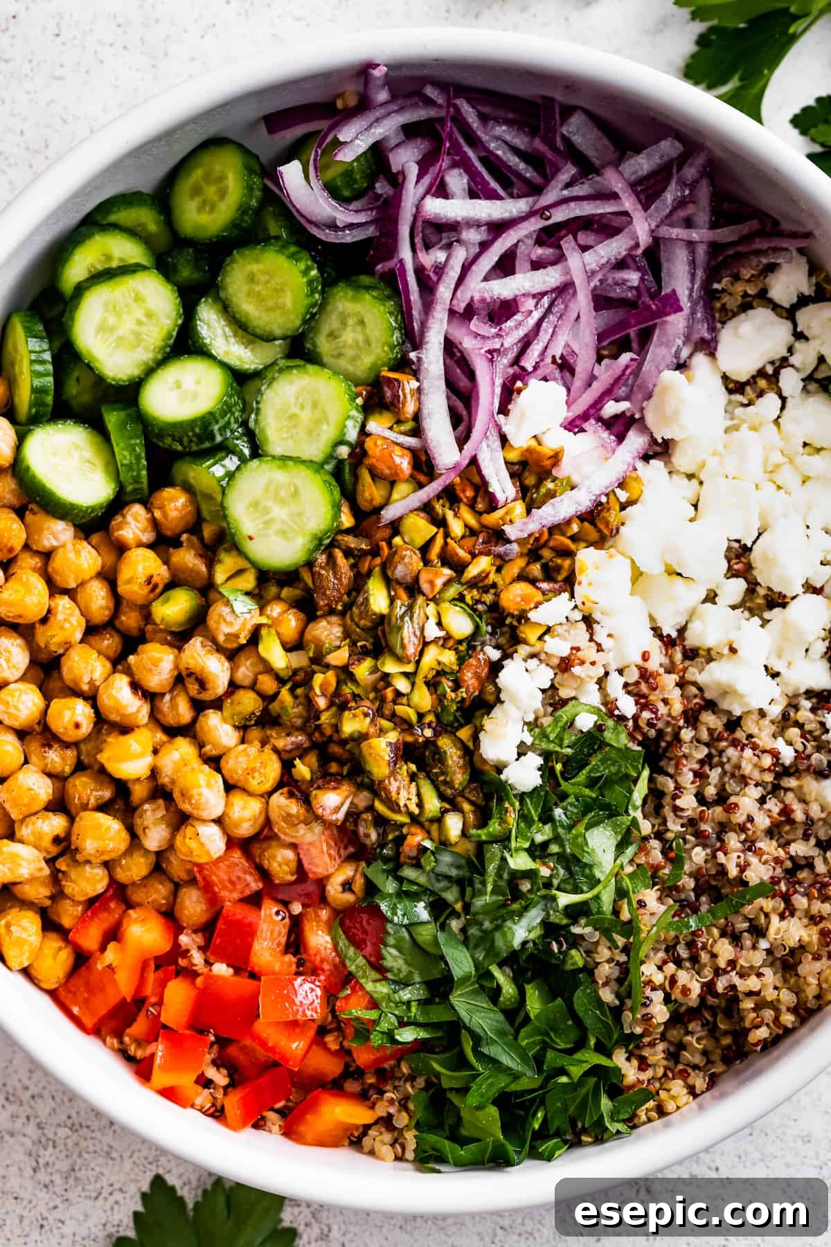 A vibrant Jennifer Aniston salad in a large bowl, featuring a colorful mix of tri-color quinoa, pan-roasted chickpeas, crisp cucumbers, red onions, bell peppers, fresh herbs, and crumbled feta cheese.