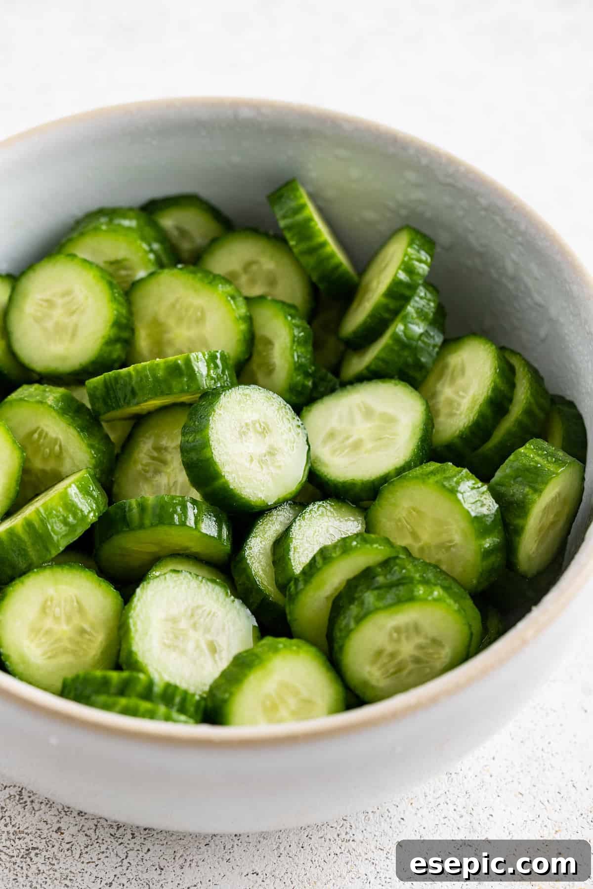Sliced cucumbers being salted in a bowl, a crucial step for achieving perfect texture in the Jennifer Aniston salad.