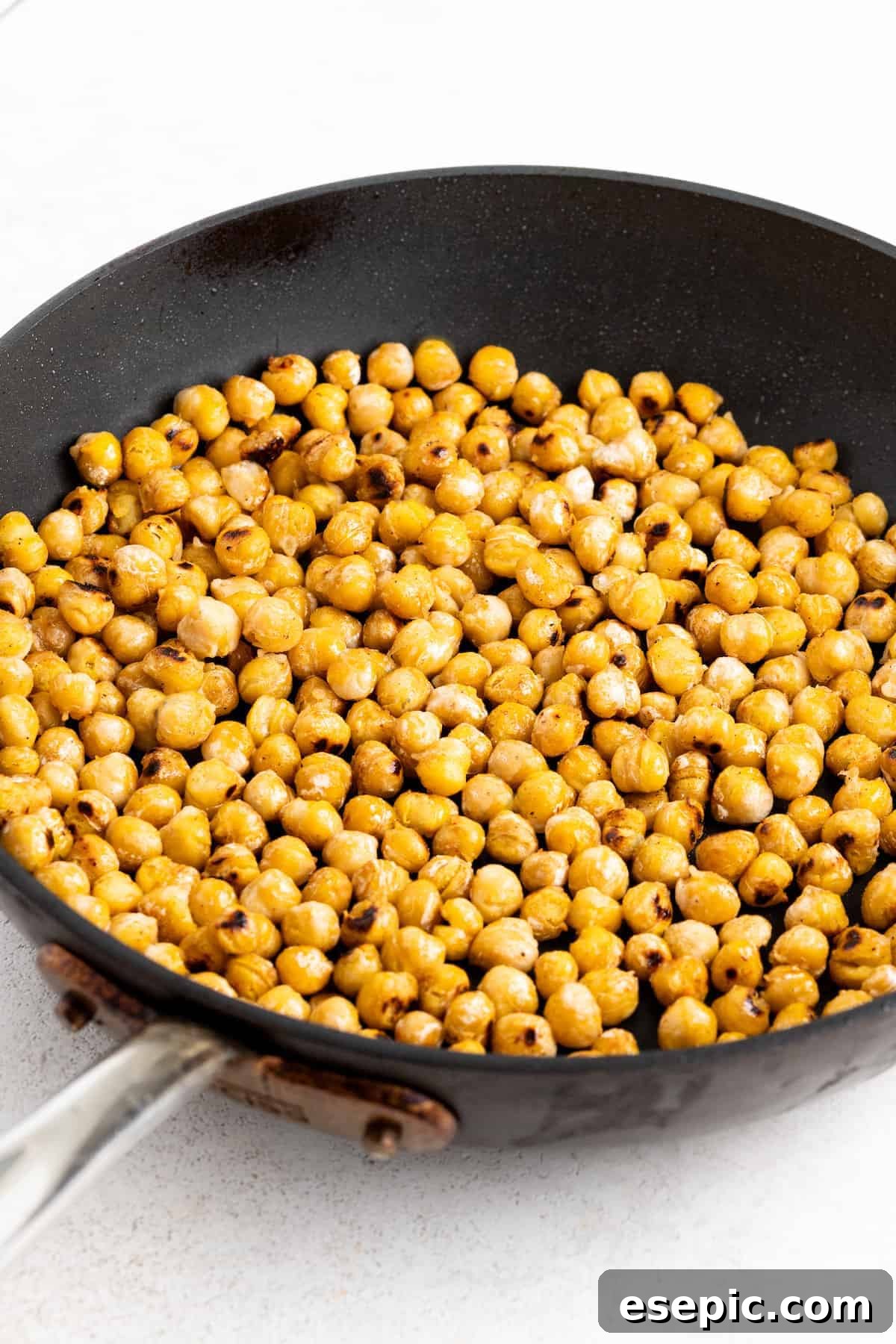 Chickpeas pan-roasting in a skillet until golden and crispy, adding a delightful crunch to the Jennifer Aniston salad.