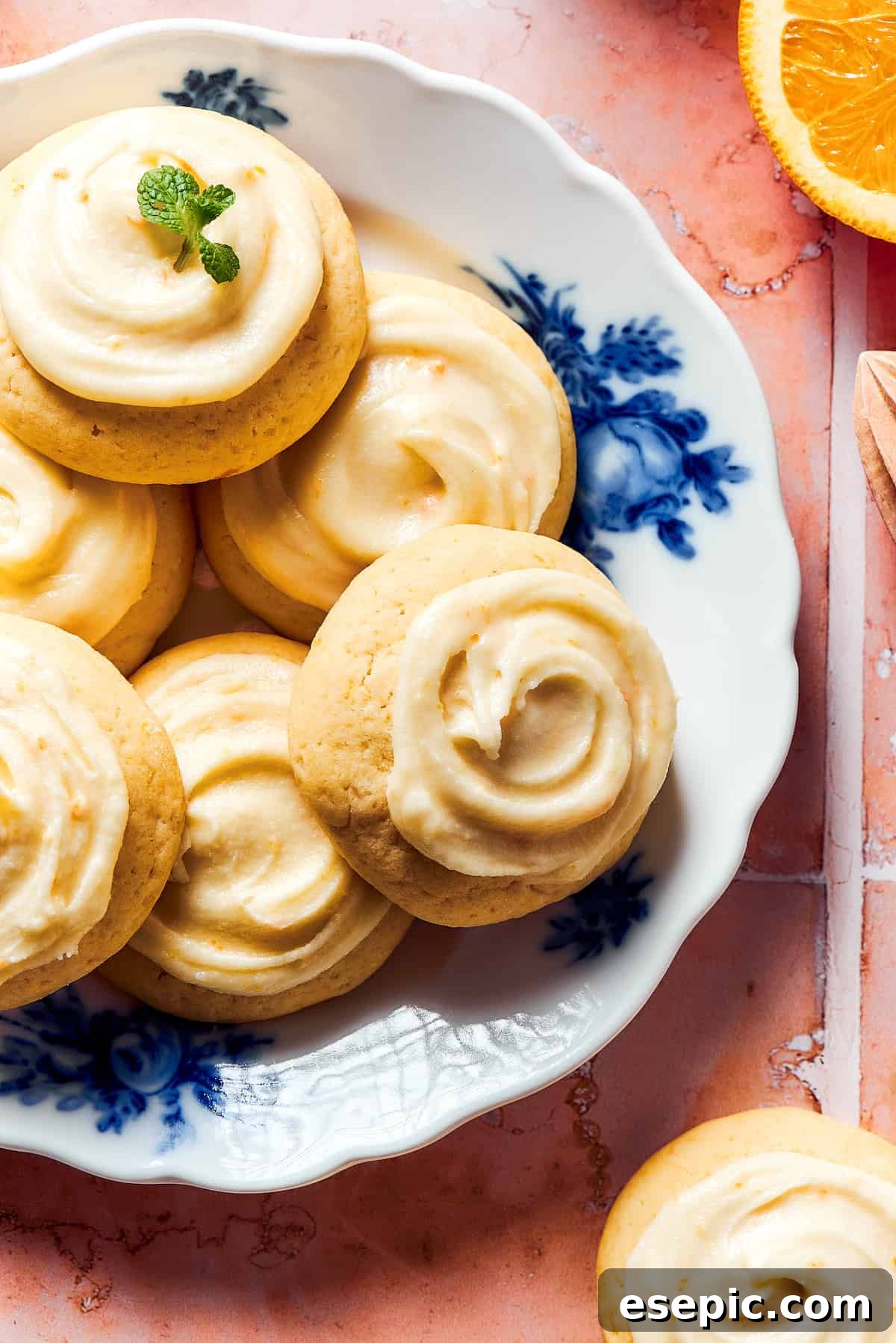 Sweet, buttery Orange Cookies have a light citrus taste and pretty pastel color - perfect for parties, cookie swaps, baby showers, and more! A blue and white flowered plate with iced orange cookies.