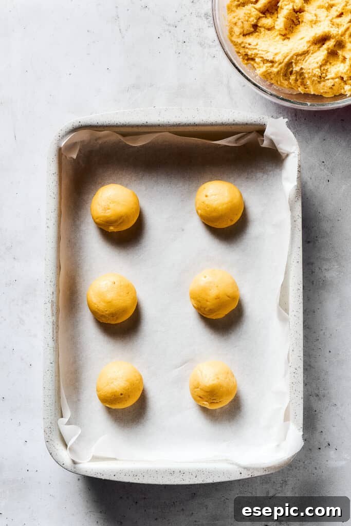 Sweet, buttery Orange Cookies have a light citrus taste and pretty pastel color - perfect for parties, cookie swaps, baby showers, and more! Balls of cookie dough on a parchment-lined baking sheet.