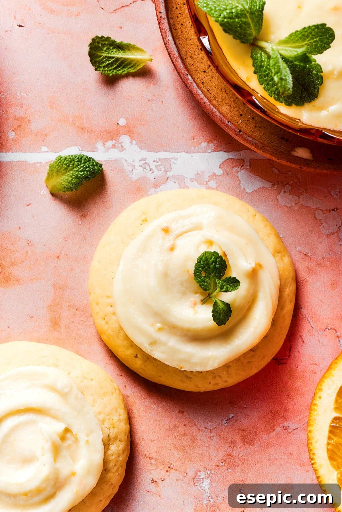 Sweet, buttery Orange Cookies have a light citrus taste and pretty pastel color - perfect for parties, cookie swaps, baby showers, and more! Three orange cookies garnished with fresh herbs, on a tile table.