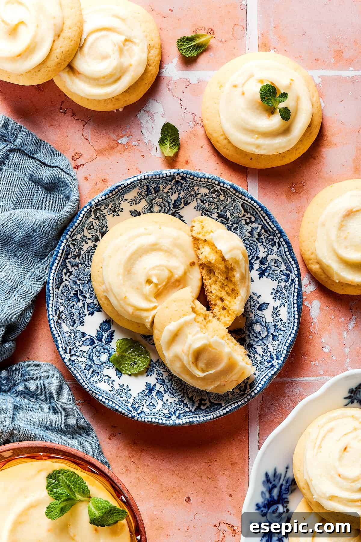 Sweet, buttery Orange Cookies have a light citrus taste and pretty pastel color - perfect for parties, cookie swaps, baby showers, and more! Cookies laid out on a tiled table, with some cookies on a plate.