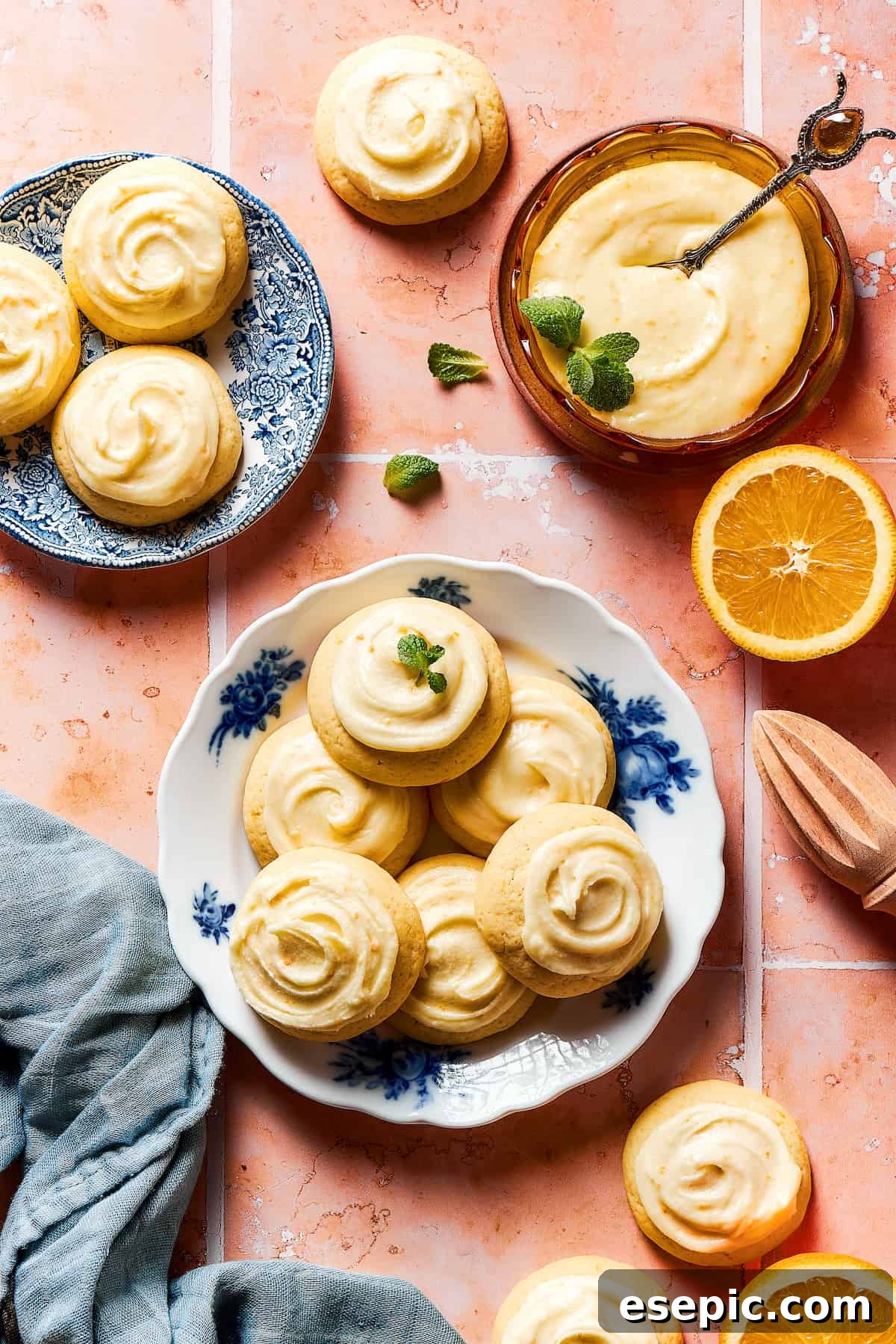 Sweet, buttery Orange Cookies have a light citrus taste and pretty pastel color - perfect for parties, cookie swaps, baby showers, and more! A platter of iced cookies with more cookies on a small saucer.