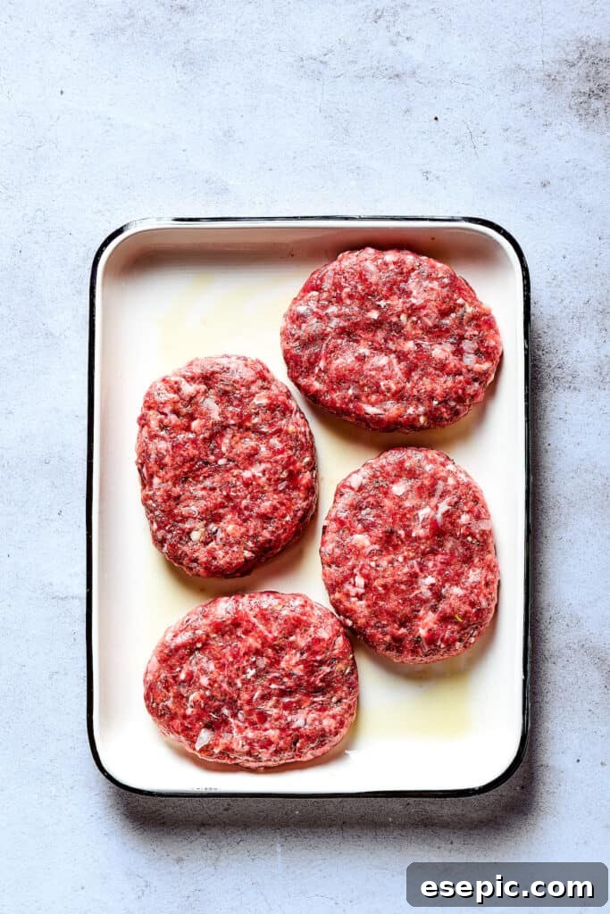 Six perfectly shaped raw beef patties resting on a baking sheet, ready for cooking.