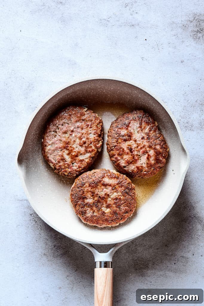 Browned Salisbury steak patties sizzling in a skillet, displaying a delicious sear.