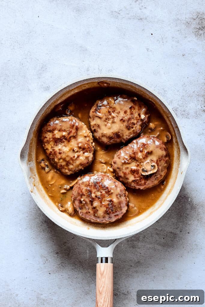The finished Salisbury steak dish in a skillet, with beef patties covered in gravy, garnished and ready to be served.