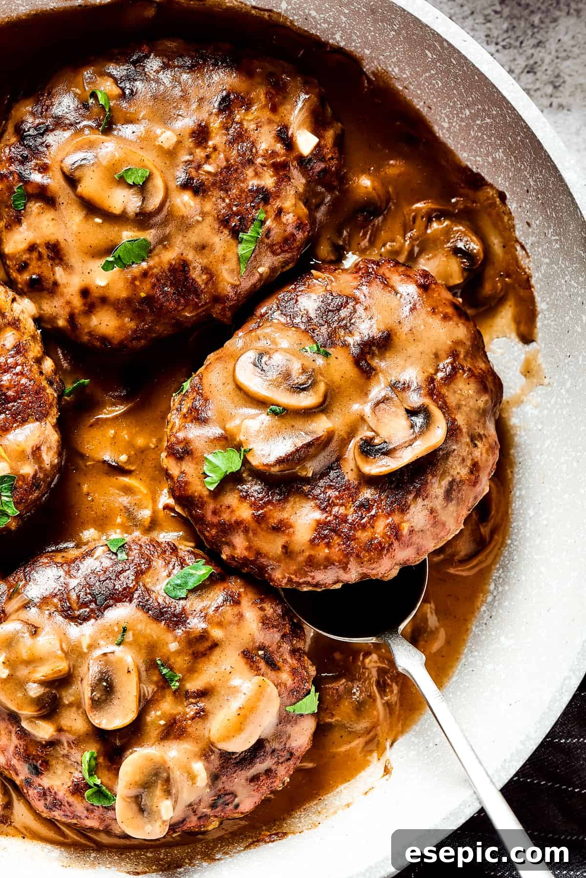 A close-up of a bubbling skillet filled with Salisbury steaks and a generous amount of mushroom and onion gravy, ready to serve.