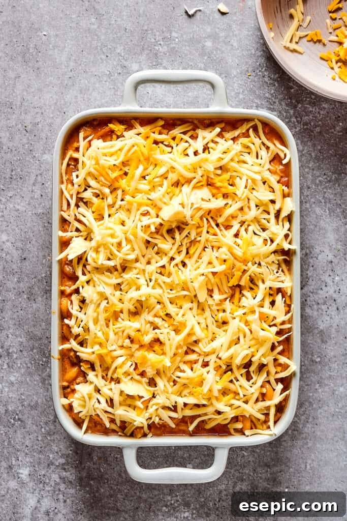 A baking dish filled with the cheeseburger casserole base, generously topped with an even layer of shredded cheese.