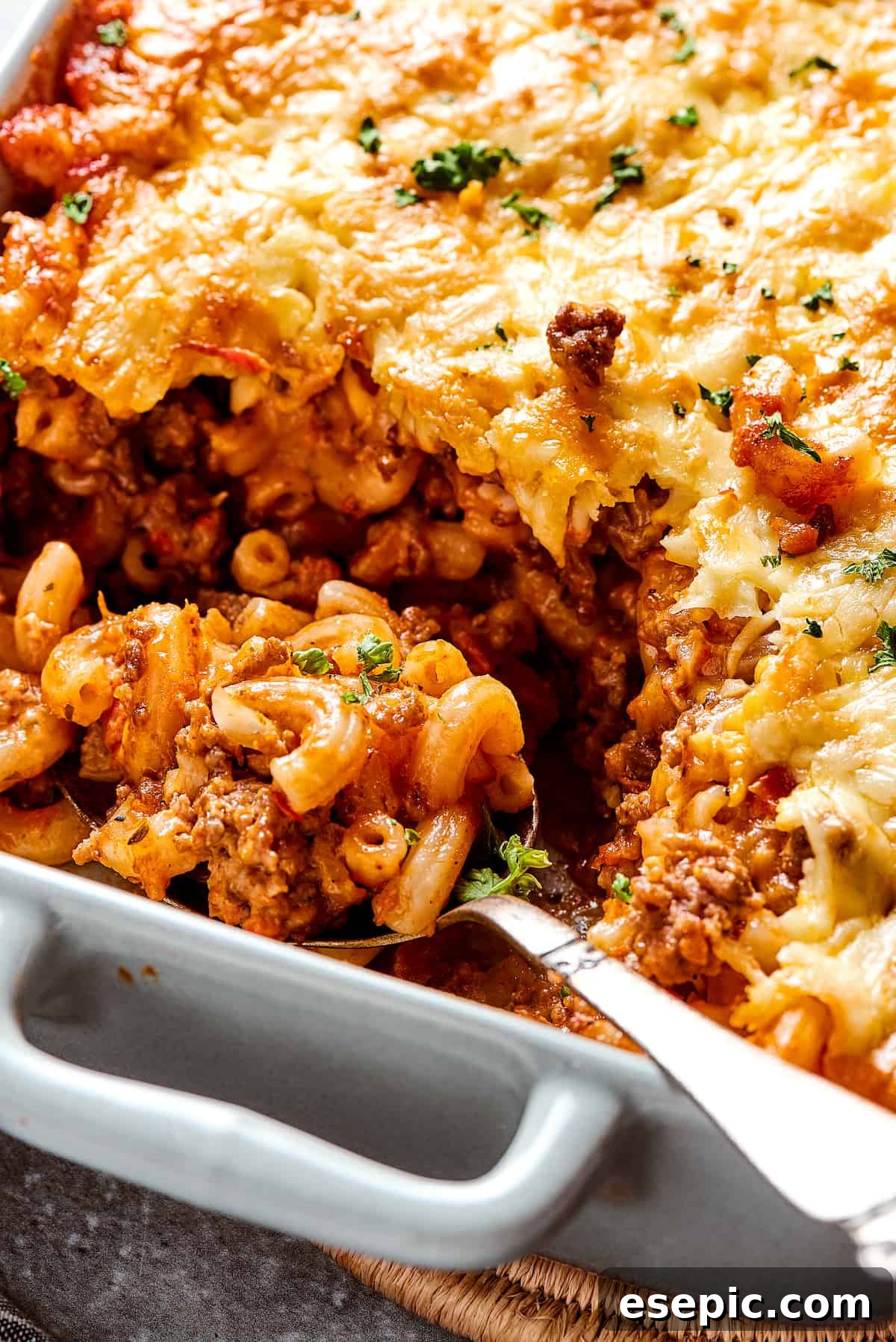A comforting cheeseburger casserole with a portion already scooped out, revealing the creamy pasta and beef, with a serving spoon resting in the dish.