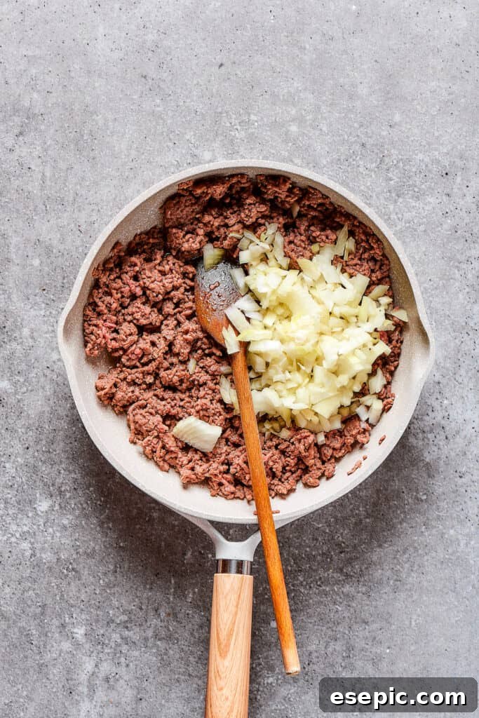 Adding diced onion to a skillet of sizzling ground beef for the cheeseburger casserole.
