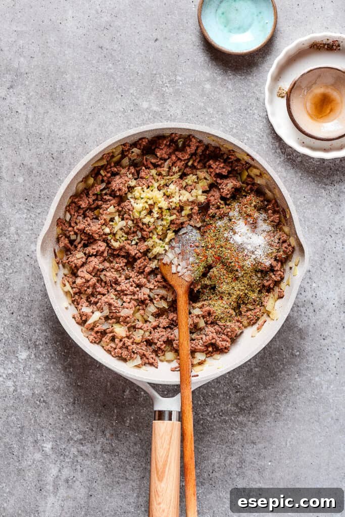 Seasoning a skillet of browned beef and onions with a medley of aromatic spices.