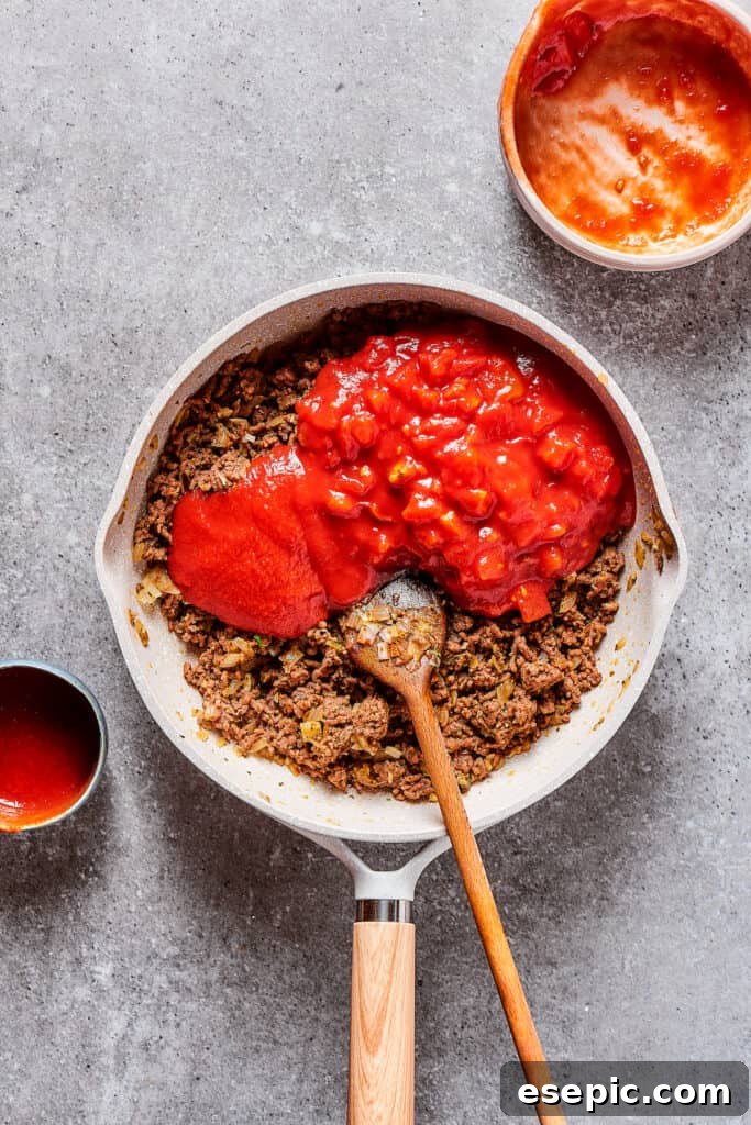 Combining tomato puree and diced tomatoes with the savory ground beef in a large skillet.