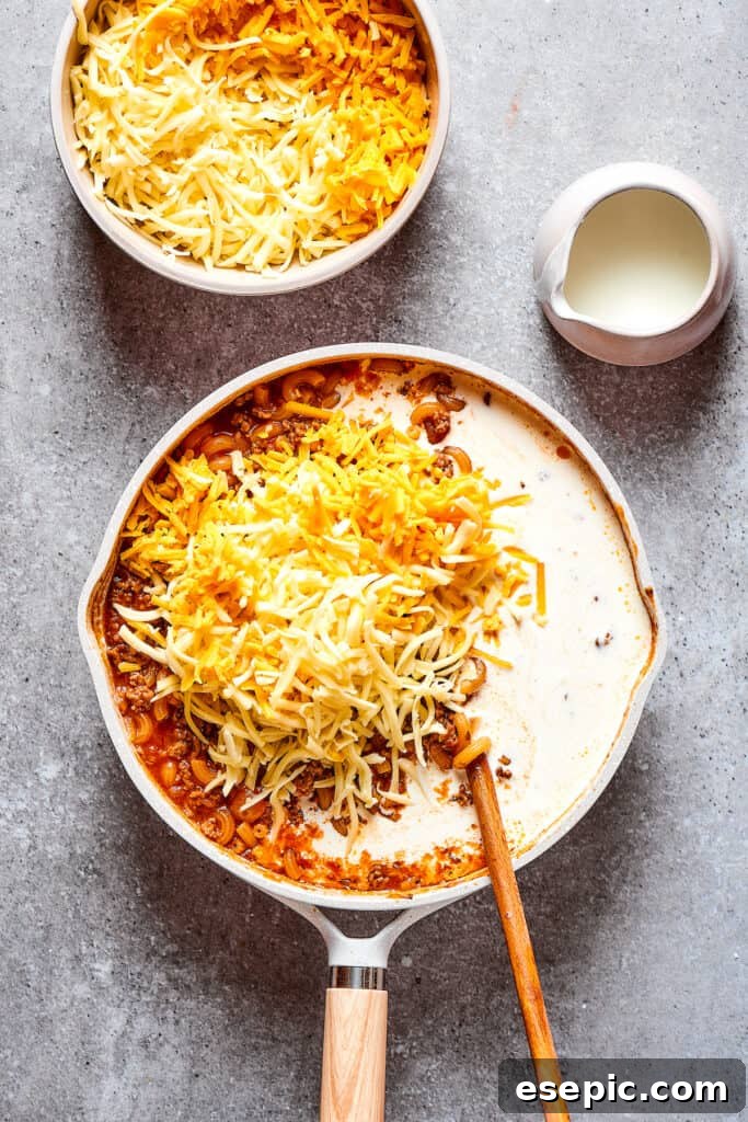 Stirring heavy cream and shredded cheese into the warm pasta and beef mixture for ultimate creaminess.
