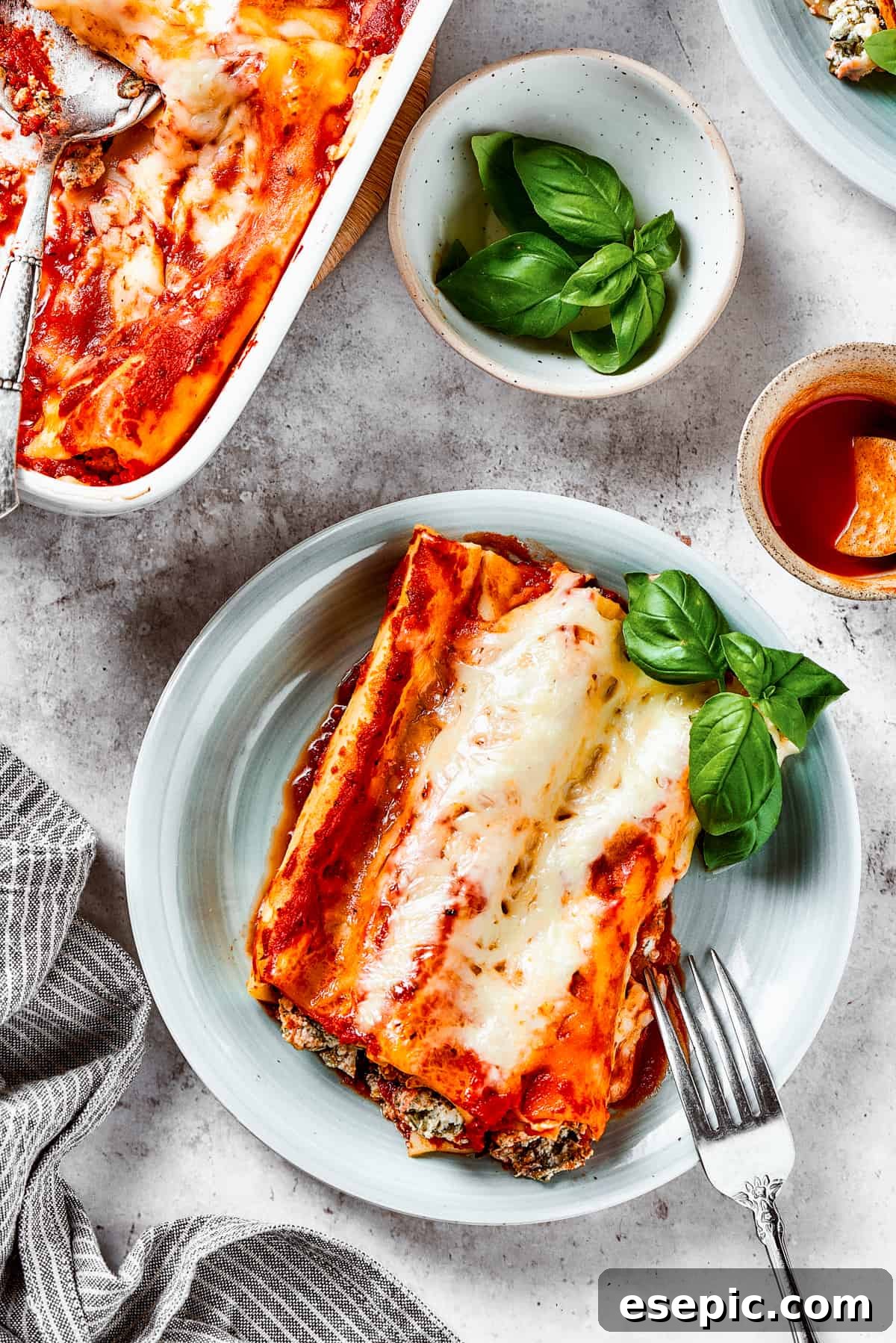 An overhead shot of stuffed manicotti on a plate, with a casserole dish and serving spoon in the background.