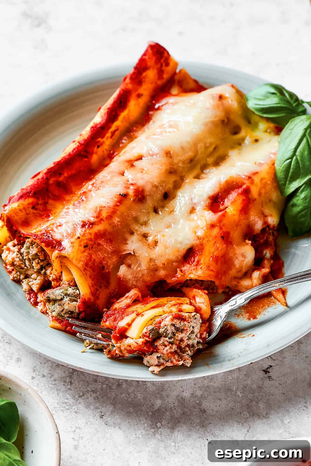 Piercing a piece of baked manicotti with a fork, revealing the soft pasta and rich filling.
