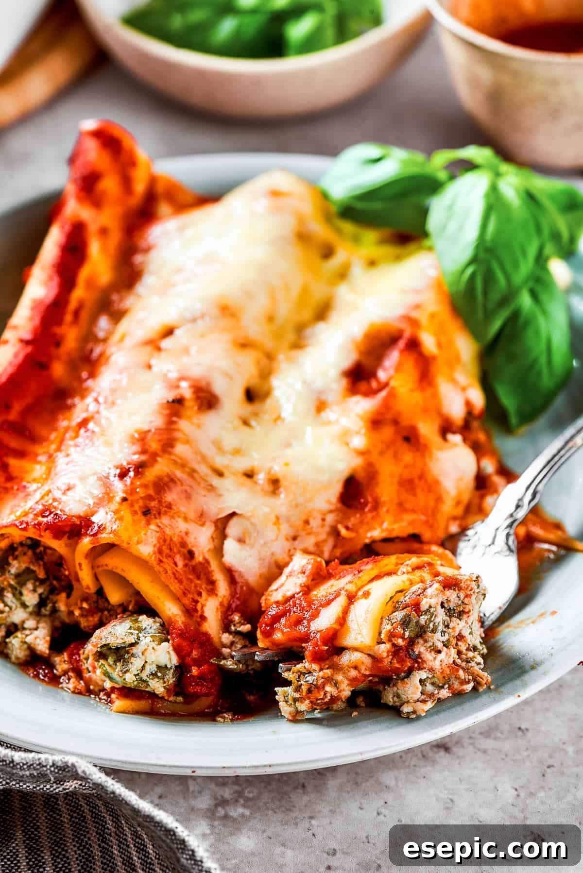 A close-up of a plate featuring three perfectly stuffed manicotti tubes, topped with melted cheese and fresh herbs.