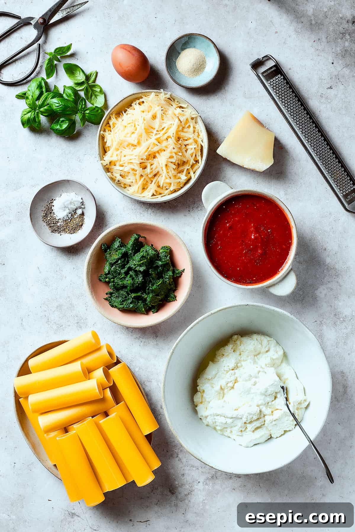 Ingredients for Stuffed Manicotti, including pasta, spinach, cheeses, and sauce, neatly arranged on a counter.