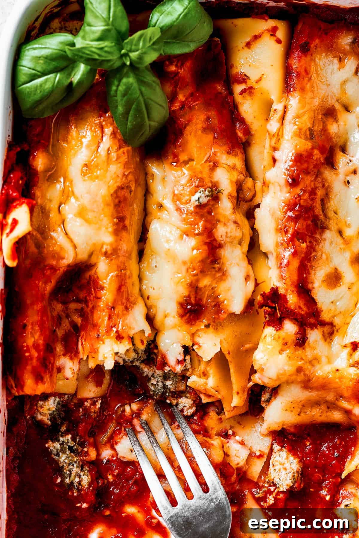A casserole dish with baked manicotti, partially served, with a serving fork resting inside.