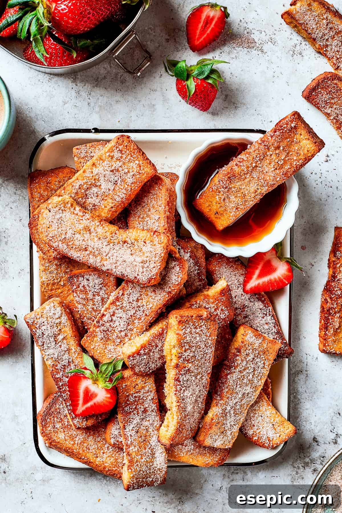 A tray of French toast sticks with maple syrup and strawberries. One stick is dunked in the syrup.