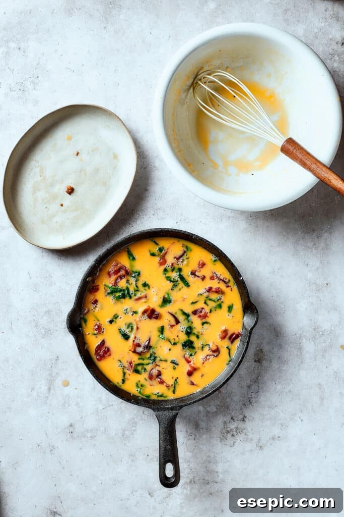 Spinach, Bacon, and Potato Frittata is a healthy, farmhouse-style dinner that's easy to make, and loaded with rich flavor. Perfect easy meal! Pouring the whisked egg mixture over the bacon, onion, spinach, and potatoes in a cast-iron pan, ready for cooking.