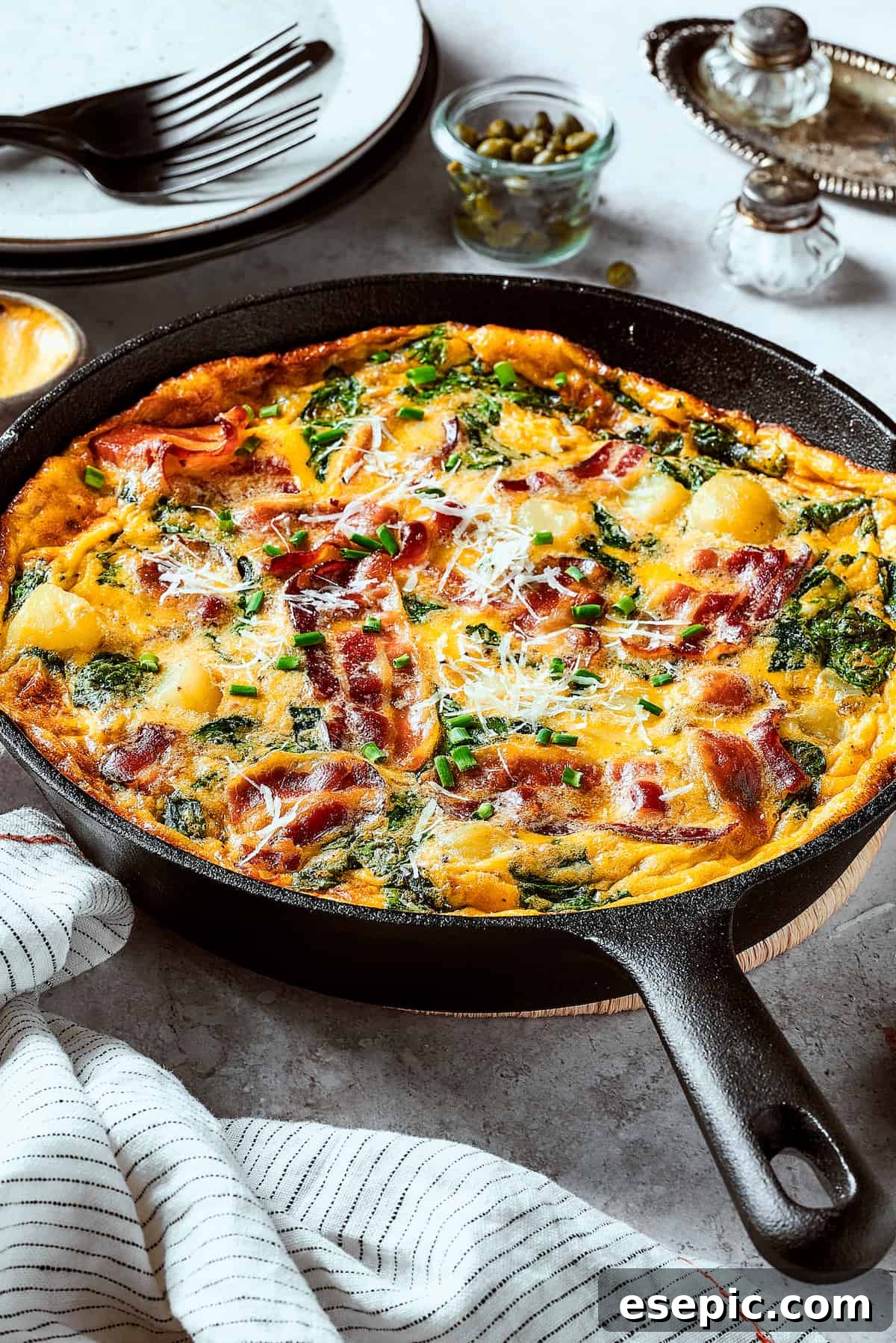 Spinach, Bacon, and Potato Frittata is a healthy, farmhouse-style dinner that's easy to make, and loaded with rich flavor. Perfect easy meal! A cast-iron skillet with a freshly baked, golden-brown egg dish in it, ready for serving.