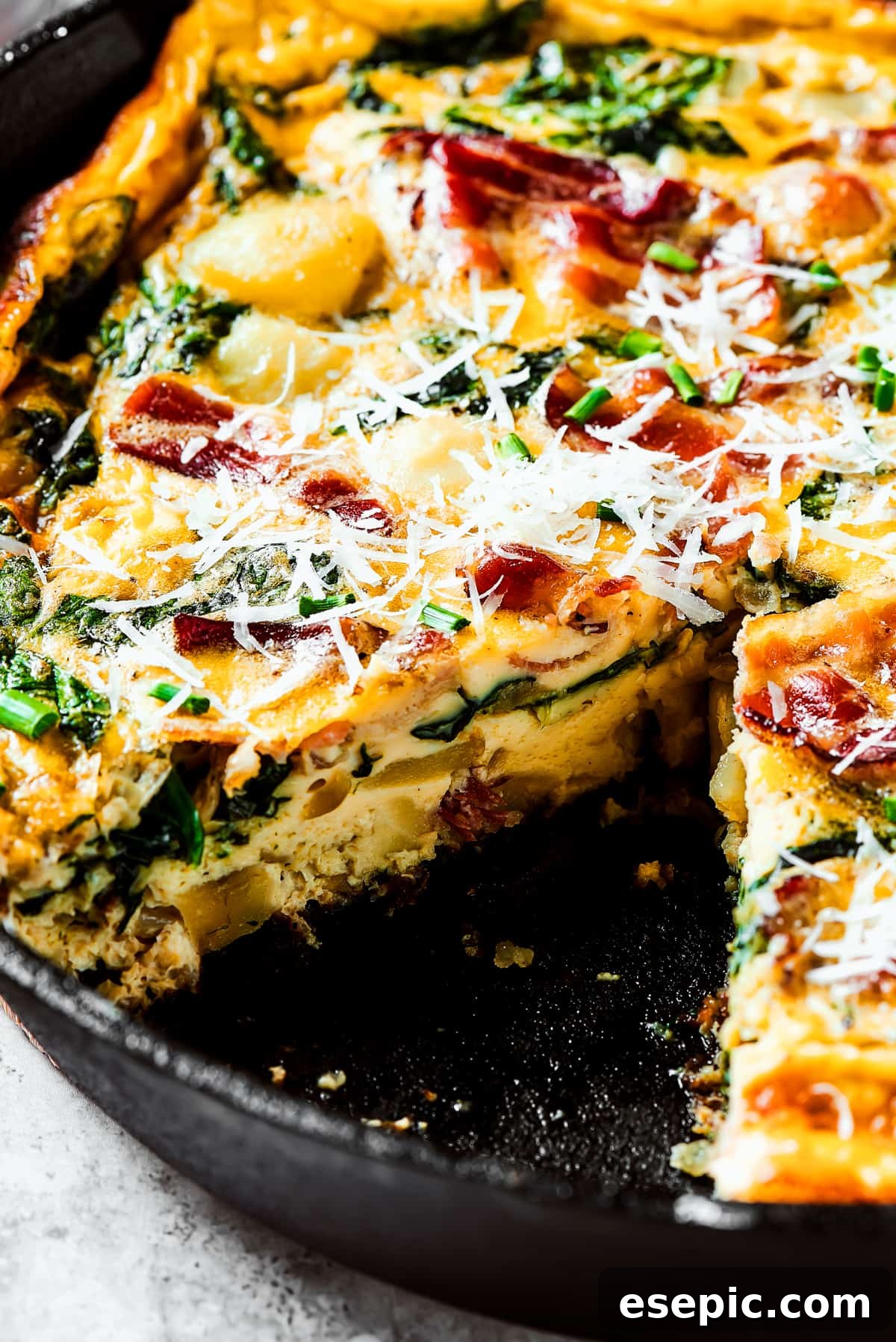 Spinach, Bacon, and Potato Frittata is a healthy, farmhouse-style dinner that's easy to make, and loaded with rich flavor. Perfect easy meal! A baked frittata in a cast-iron skillet with one slice already removed, showing the hearty fillings.