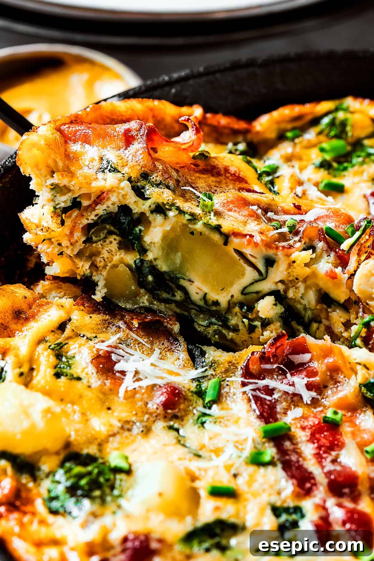 Spinach, Bacon, and Potato Frittata is a healthy, farmhouse-style dinner that's easy to make, and loaded with rich flavor. Perfect easy meal! Lifting a golden-brown slice of frittata out of a cast-iron pan with a spatula, revealing its layered ingredients.