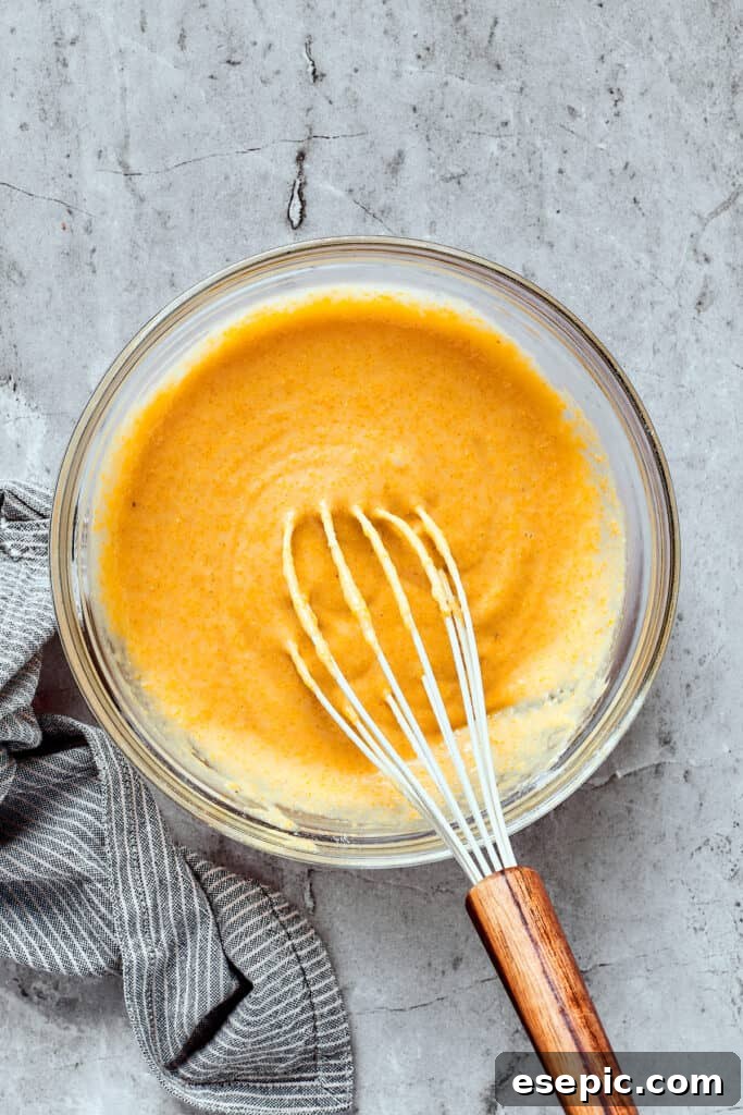 Yellow cornbread batter in a mixing bowl with a whisk.
