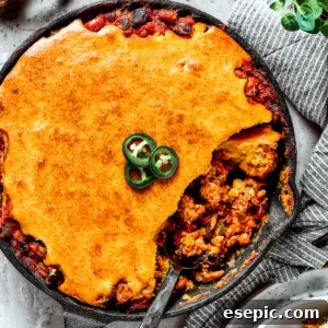 Overhead shot of a cast iron skillet with homemade Chili Cornbread Casserole and a serving removed with a spoon.