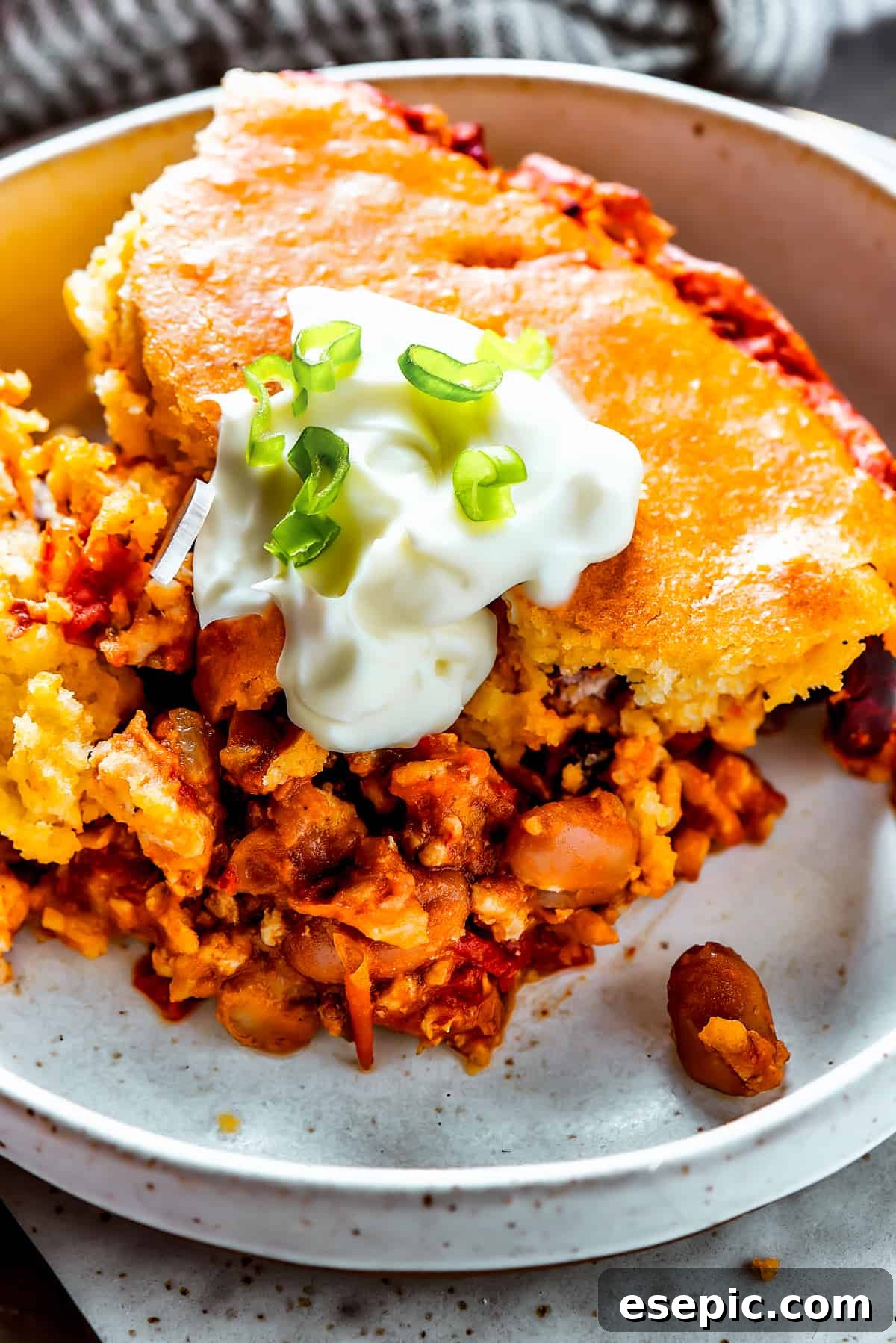 Chili cornbread casserole on a dinner plate with sour cream and scallion.