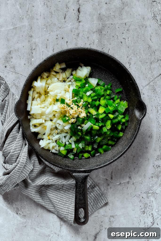 Onion, bell pepper, and garlic cooking in a cast-iron skillet.