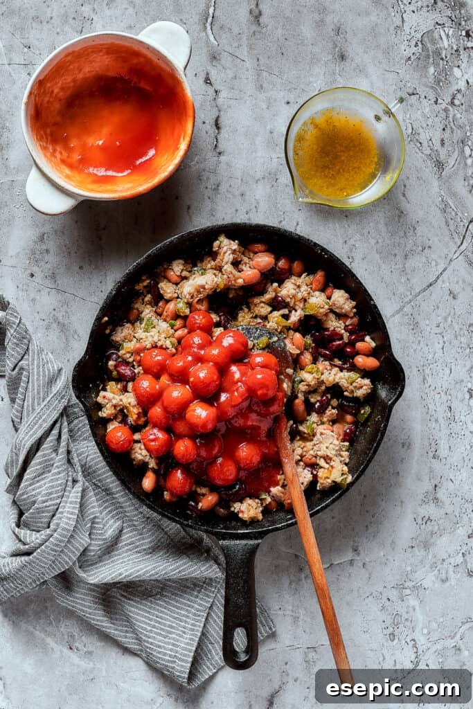 Adding tomatoes and other chili ingredients to a skillet.