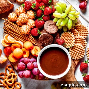 A dessert board with fruit, waffles, pretzels, and with a bowl of fondue in the center.