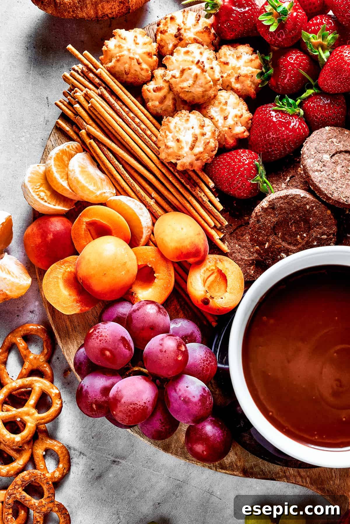 A rustic wooden charcuterie board showcasing a variety of sweet and savory dippers surrounding a bowl of rich chocolate sauce.