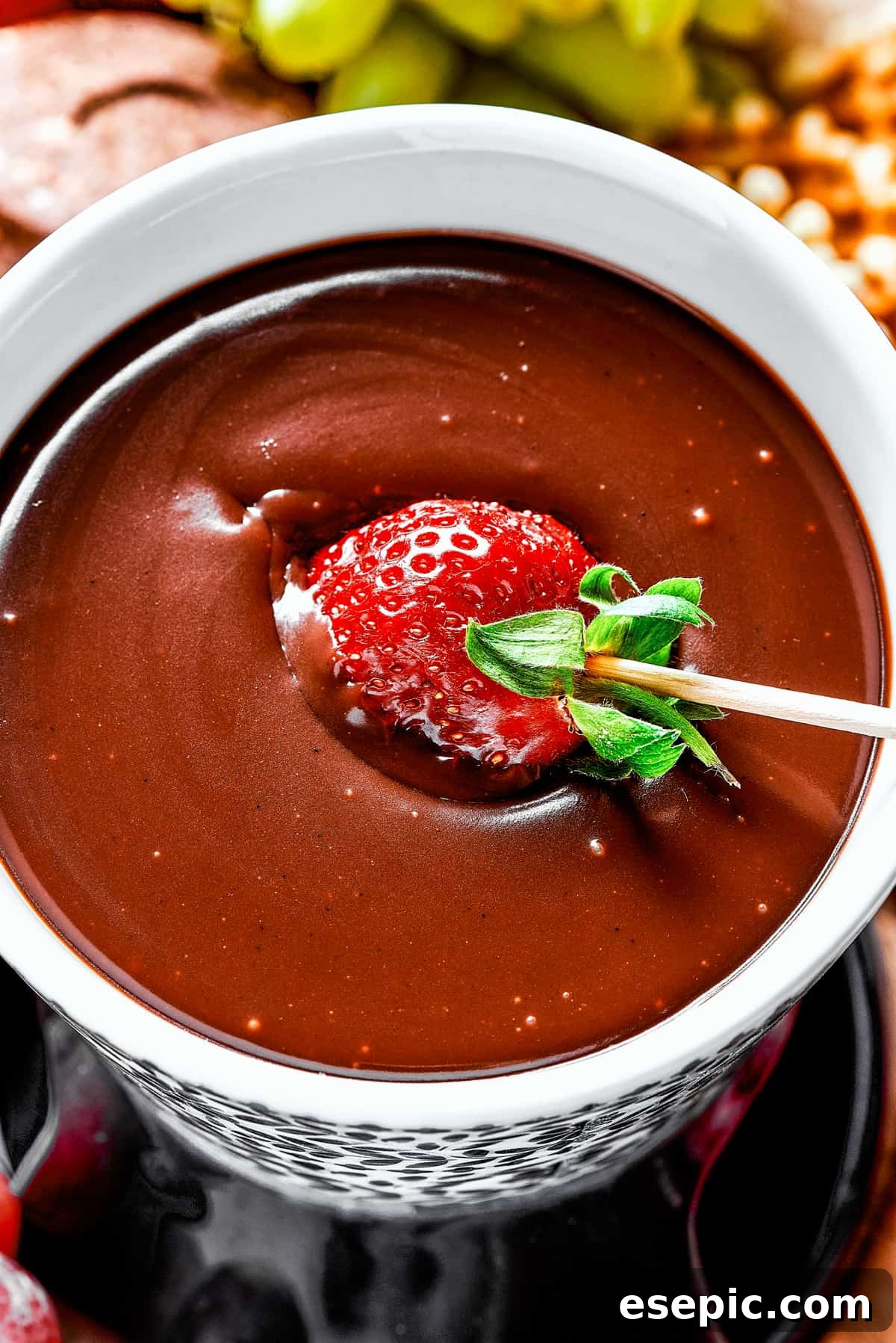 A hand dipping a vibrant red strawberry into a swirling pool of rich, melted chocolate fondue.