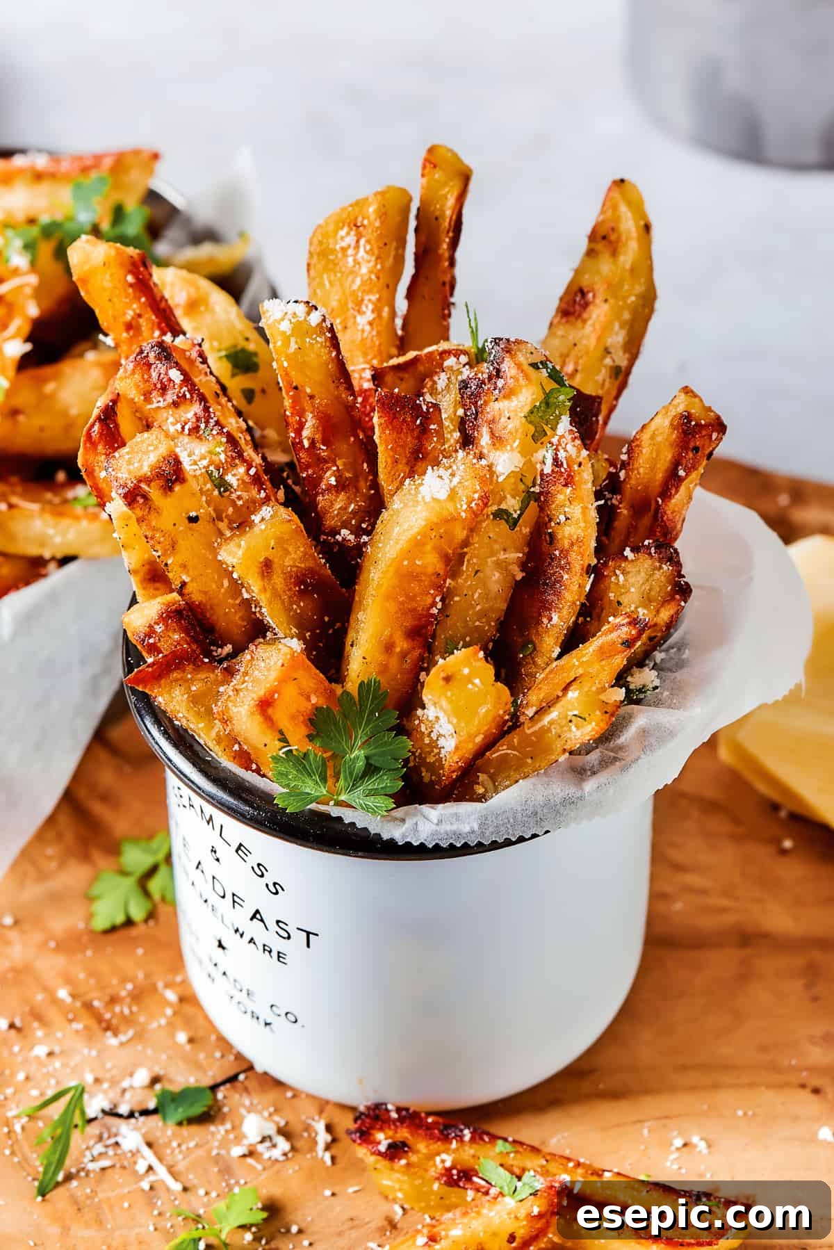 A serving of fries is stacked upright in a large white tin mug.
