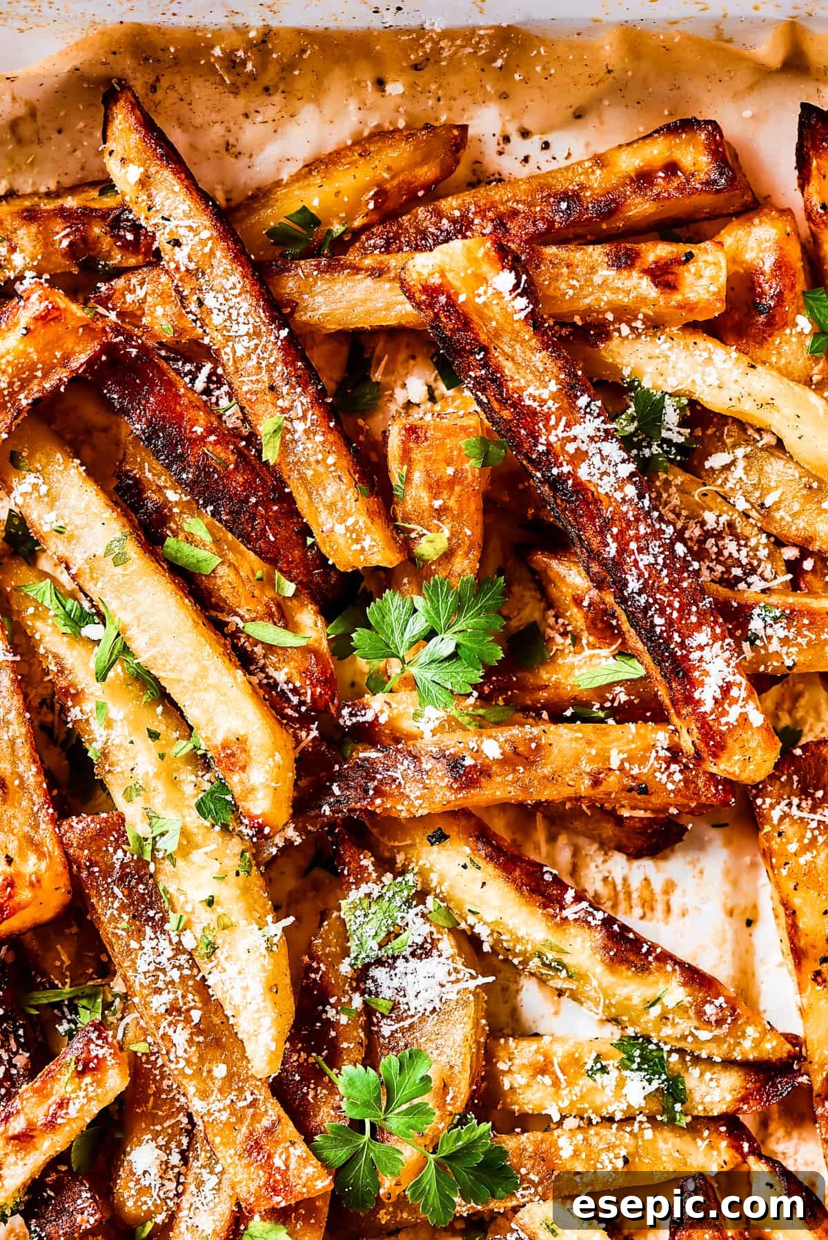 Close-up shot of seasoned garlic fries on a baking sheet and sprinkled with herbs and parmesan cheese.