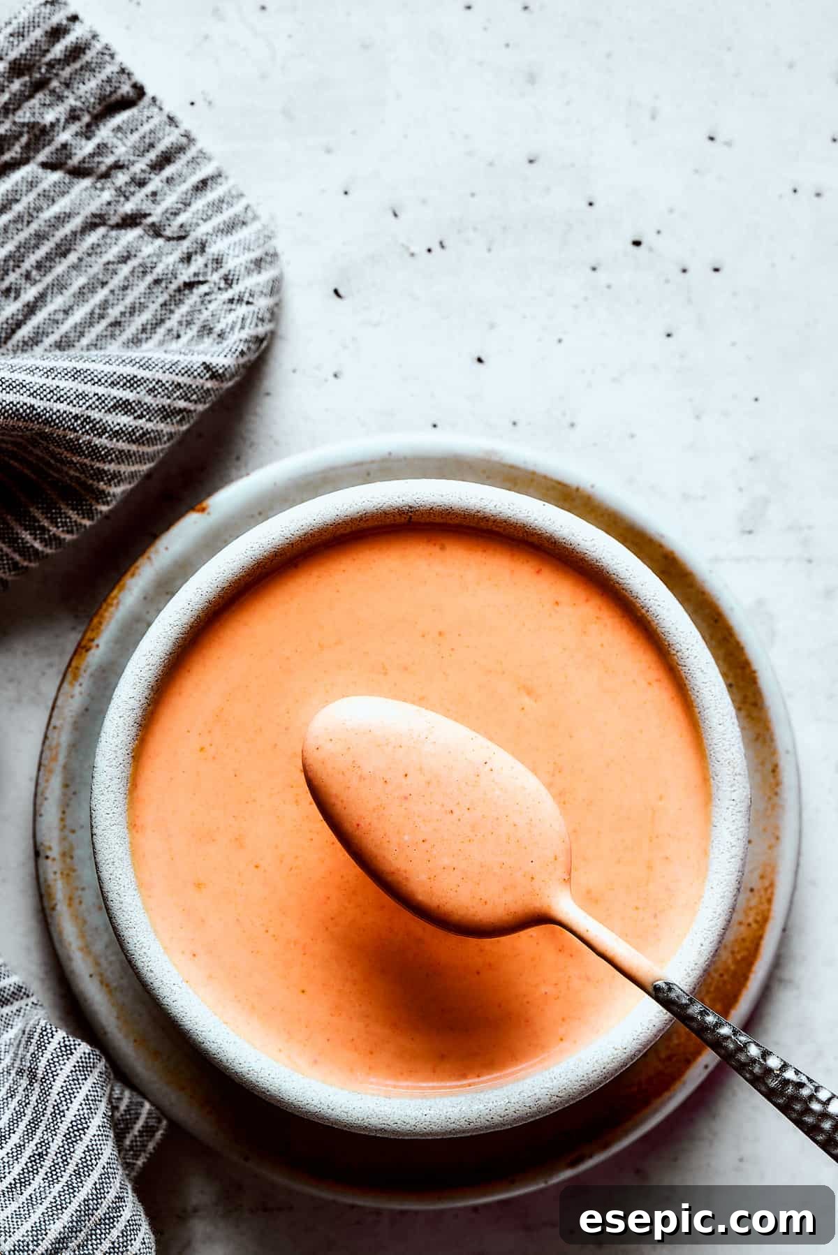 A spoonful of creamy homemade Yum Yum Sauce being lifted towards the camera, showcasing its smooth texture and appetizing color.