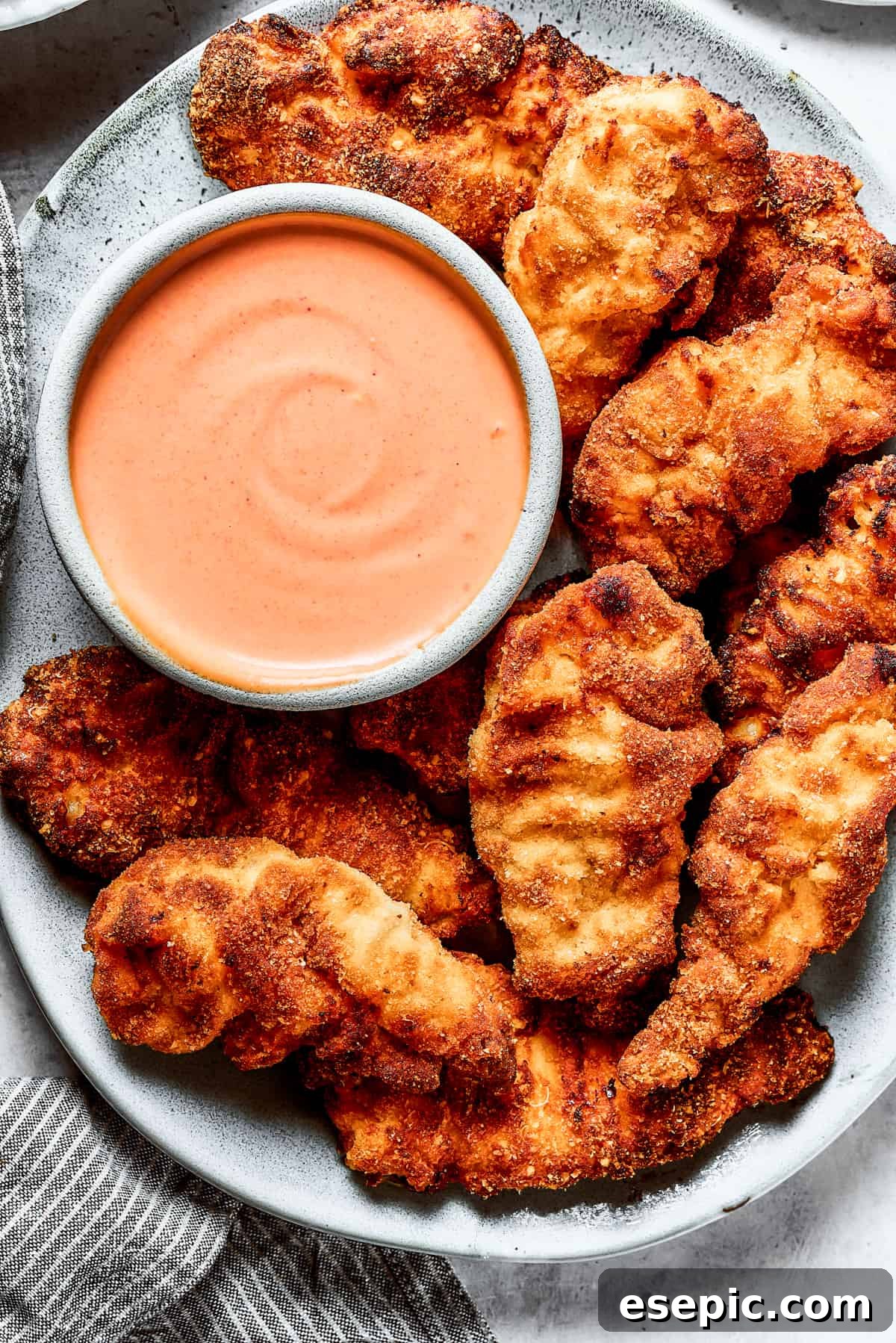 A serving platter showcasing golden-brown crispy chicken strips, accompanied by a small bowl of creamy Yum Yum Sauce, ready for a delicious meal.