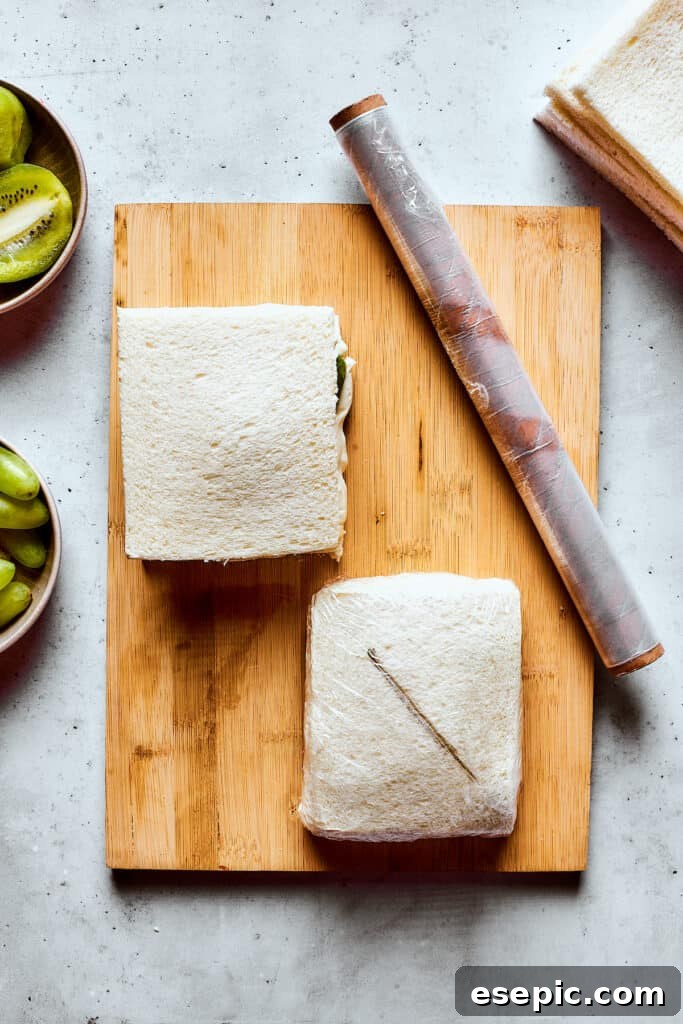 Wrapping finished fruit sandwiches tightly in plastic wrap before chilling.