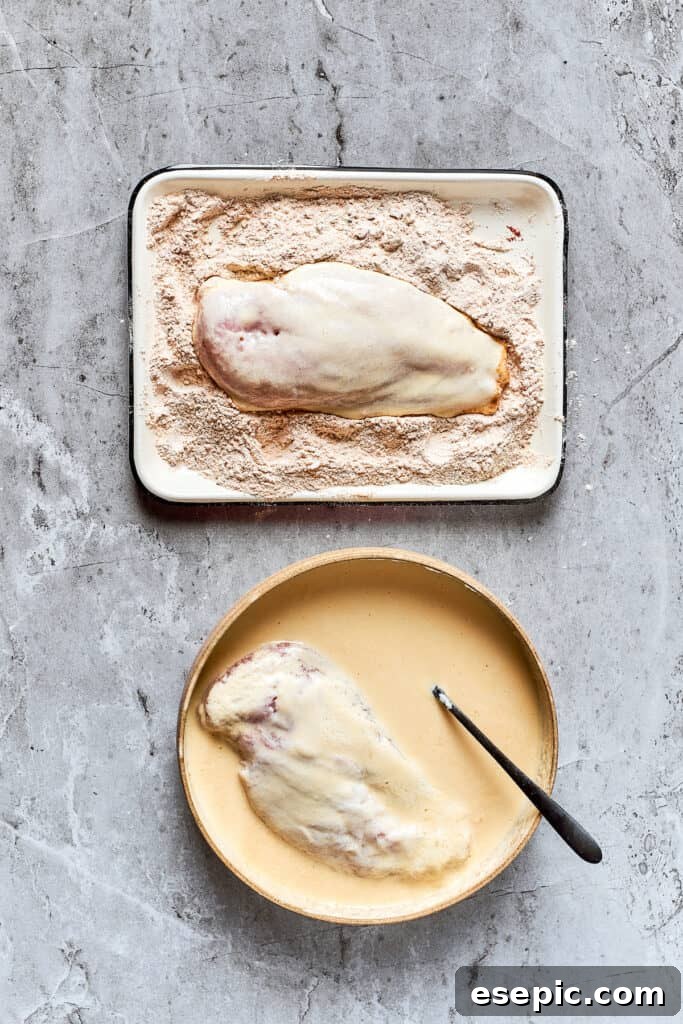 Breading chicken with seasoned flour A chicken breast being dredged in a shallow dish of seasoned flour mixture.