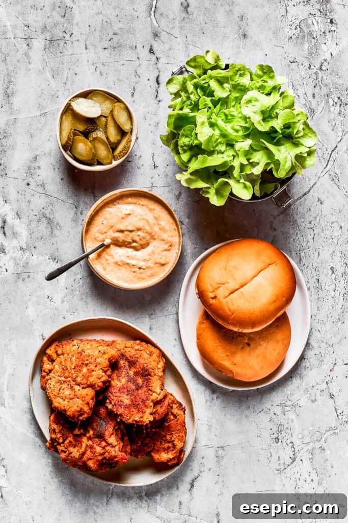 Sandwich components laid out An array of fresh ingredients for assembling the sandwich: sliced pickles, lettuce, spicy mayo, buns, and fried chicken.