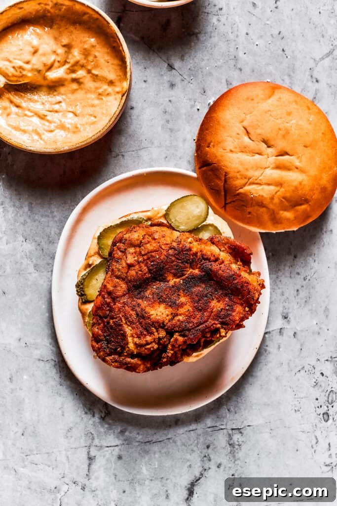 Assembling the fried chicken sandwich A hand placing a fried chicken breast onto a bun with spicy mayo and pickles, assembling the sandwich.