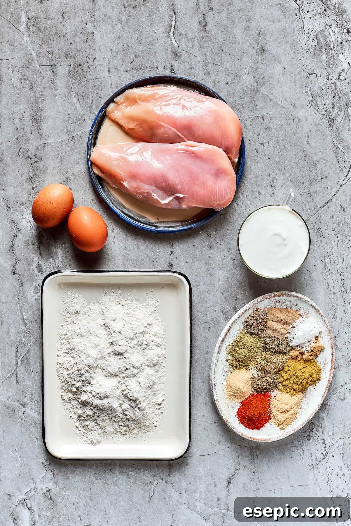Main ingredients for crispy fried chicken A visual display of the key ingredients: raw chicken breast, buttermilk, eggs, flour, and a selection of spices.