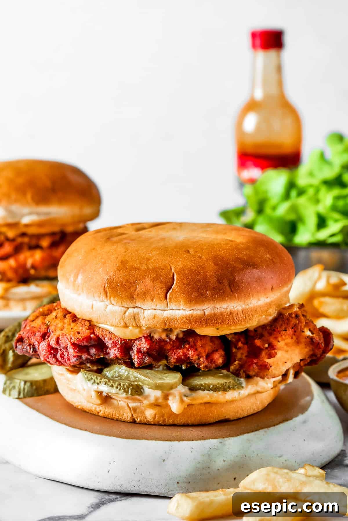 Chicken sandwich with hot sauce and sides A delicious chicken sandwich with salad and pickles, alongside a bottle of hot sauce.