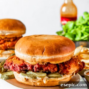 KFC-Inspired Crispy Chicken Sandwich 2 A chicken sandwich on a soft bun with salad and pickles, and a hot sauce bottle set behind the sandwich.
